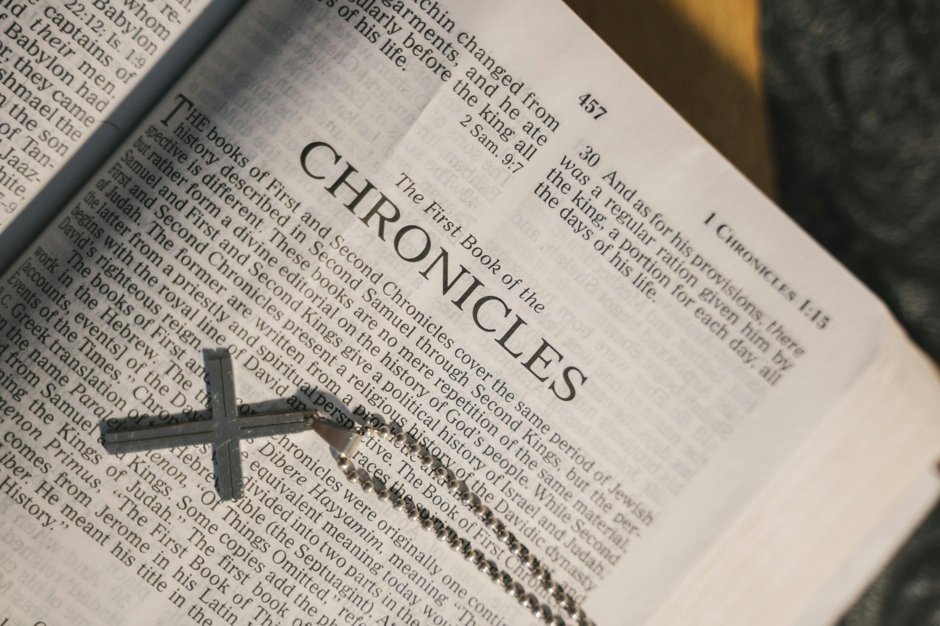 grayscale photo of a holy bible with a cross pendant